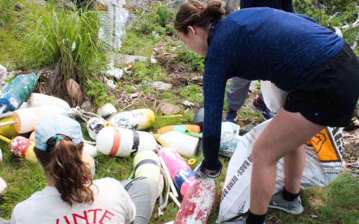 two teens pick up trash along a rocky shoreline during a service project with outward bound in maine